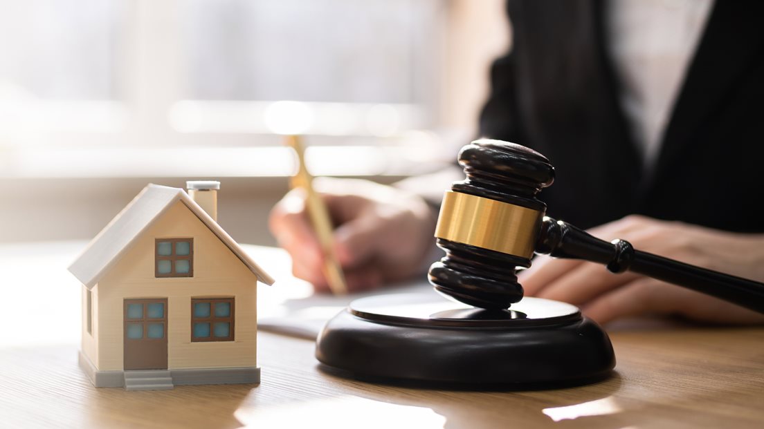 Bilde av et miniatyrhus og en dommerklubbe med en utydelig kropp i bakgrunnen.