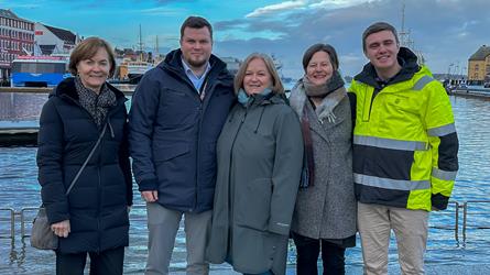 Seks voskne mennesker, tre damer og to menn, står oppstilt i Vågen i Stavanger. Alle smiler. De er kledt i vinterjakker.