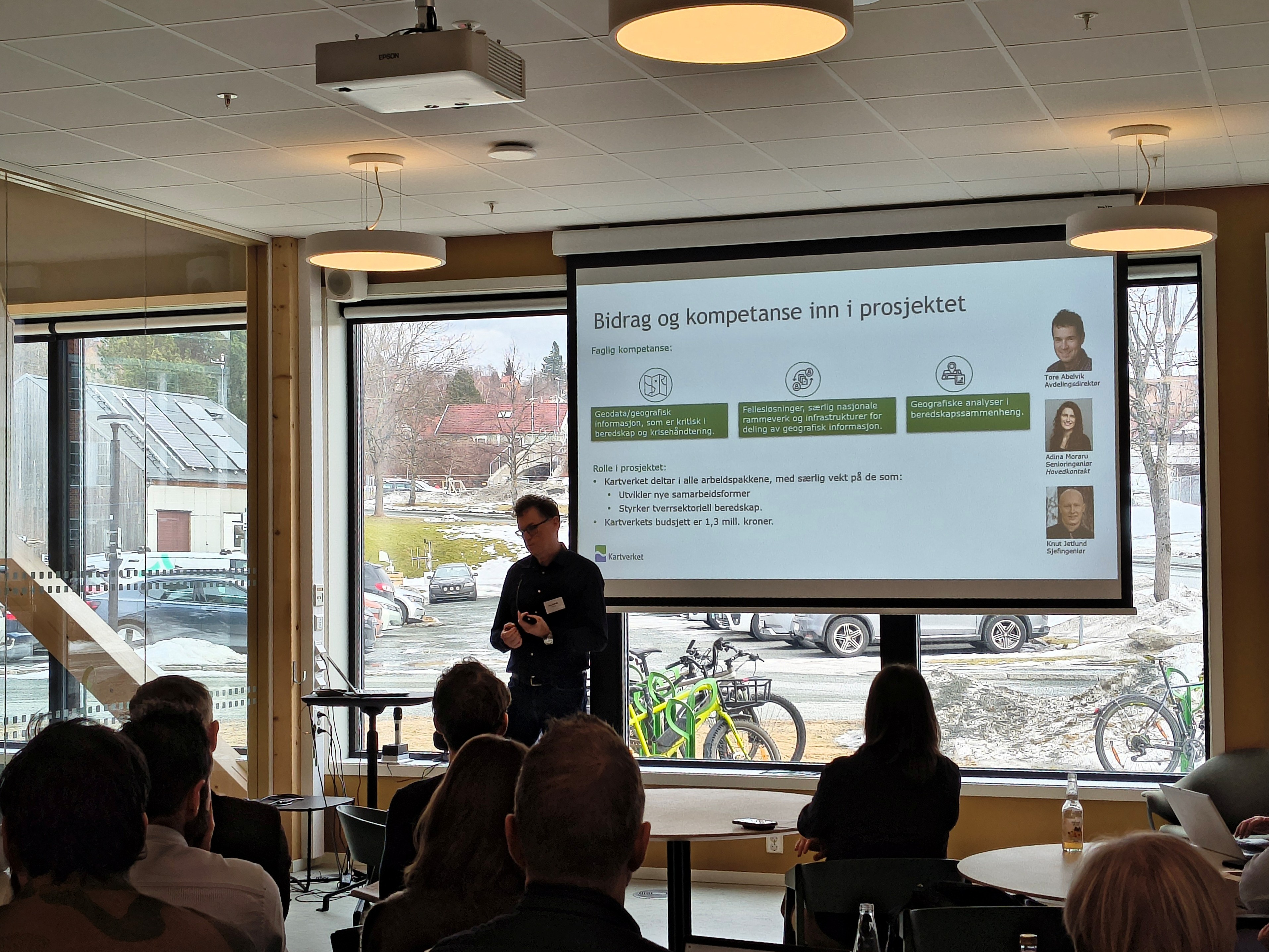 Mann med briller st&aring;r ved et lerret og presenterer noe fra Kartverket.