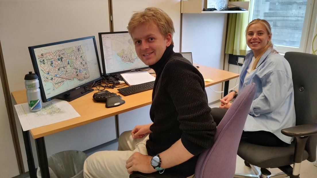 To personer sitter på et kontor med PC, tastatur m.m. foran seg