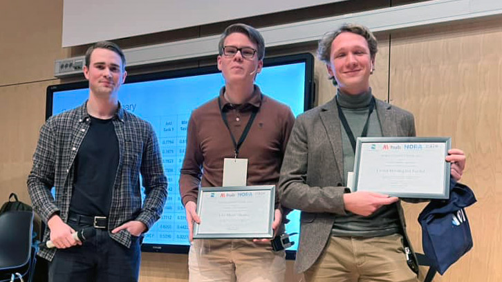 Tre unde menn st&aring;r foren en skjerm. To av dem holder hvert sitt innrammede diplom.