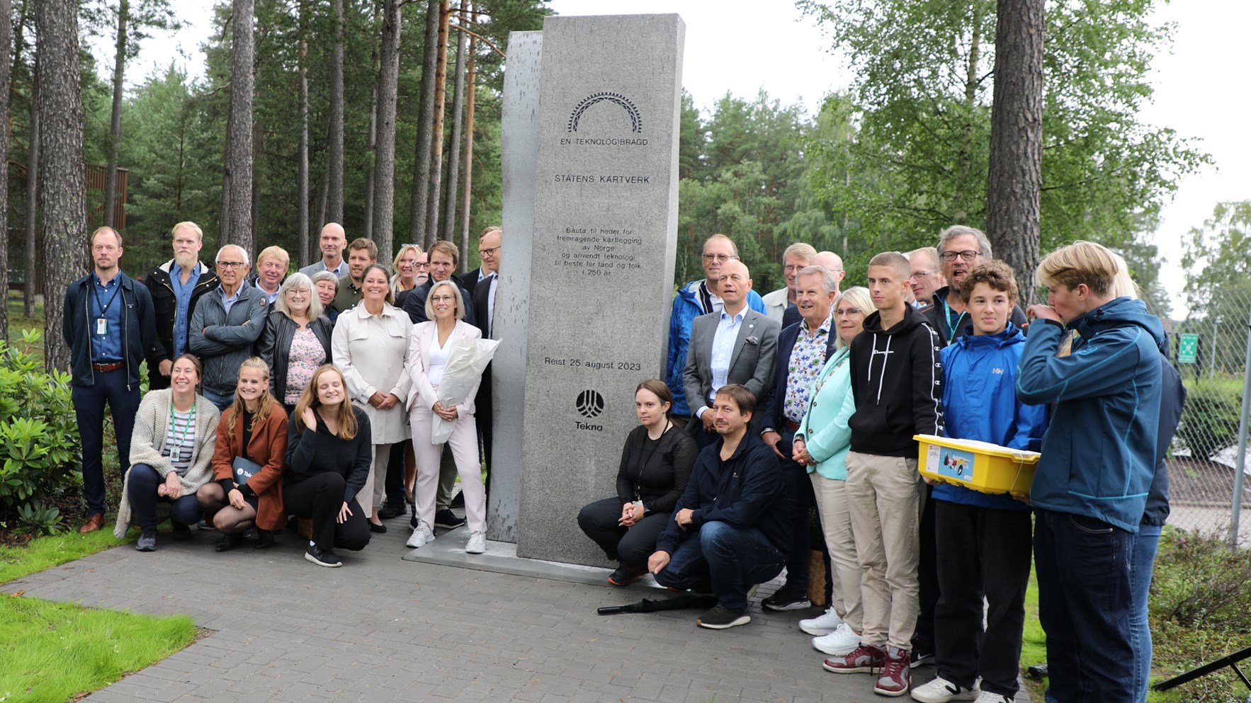 En stor gruppe mennesker står ved siden av en tre meter høy bauta utenfor Kartverkets hovedkontor.