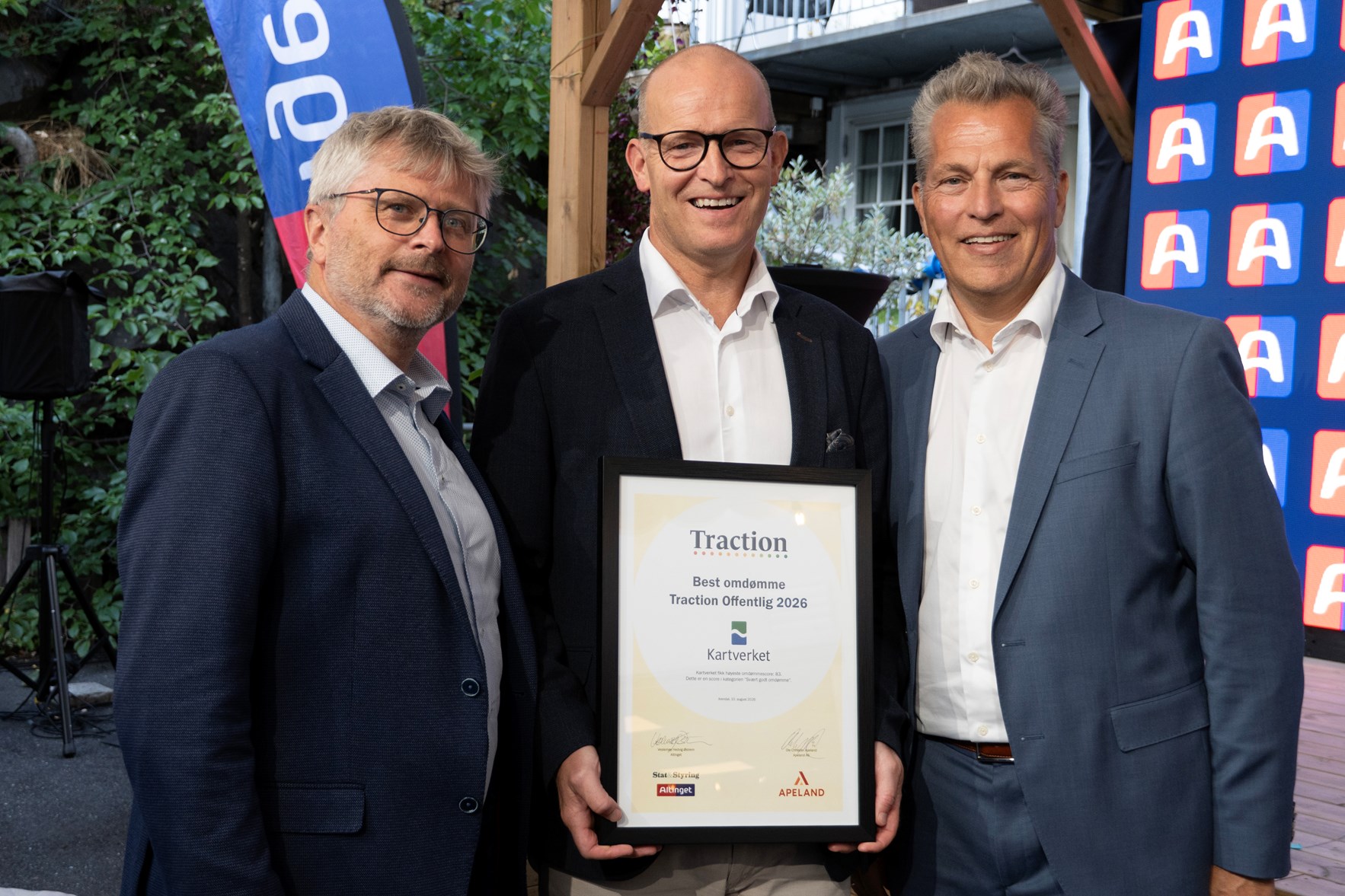 Tre personer i formelt antrekk st&aring;r sammen og holder et innrammet diplom fra Traction Offentlig 2026. Diplomet viser at Kartverket er tildelt prisen for beste omd&oslash;mme.