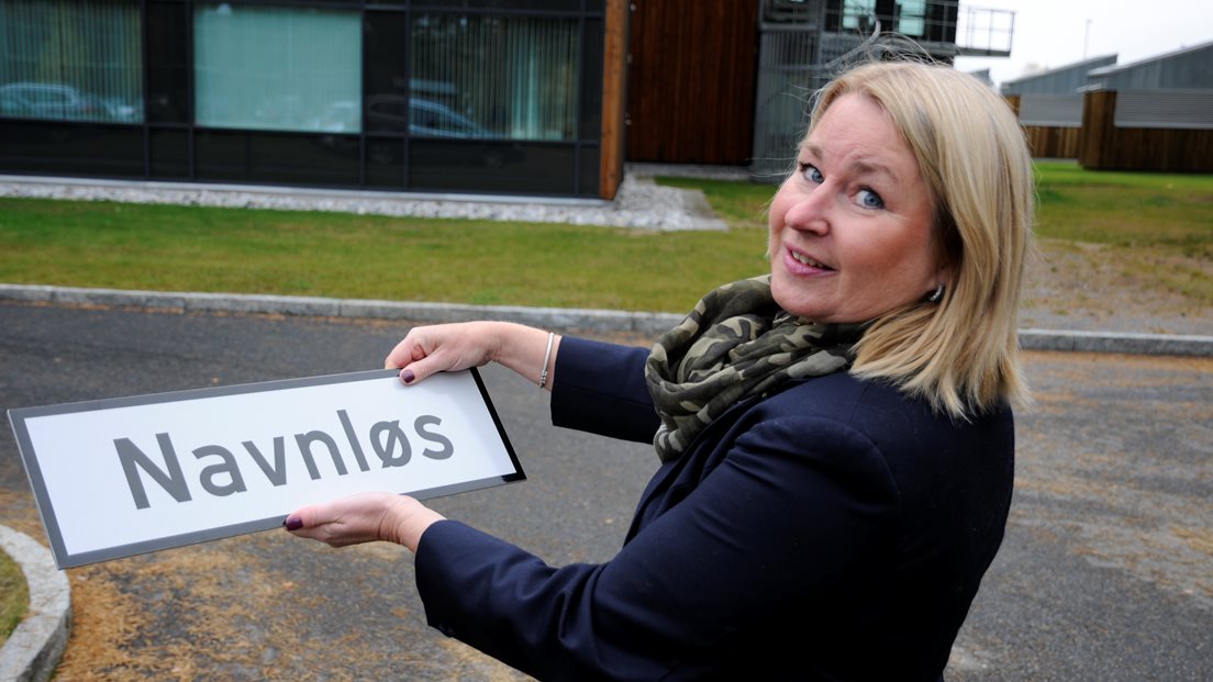 Kvinnelig kartverks-ansatt holder gateskilt med teksten "Navnløs"