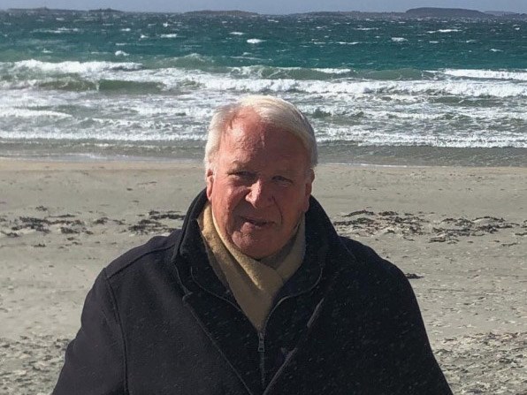 Atle Midthassel står på ei strand. Bølgene skyller innover land i bekgrunnen.