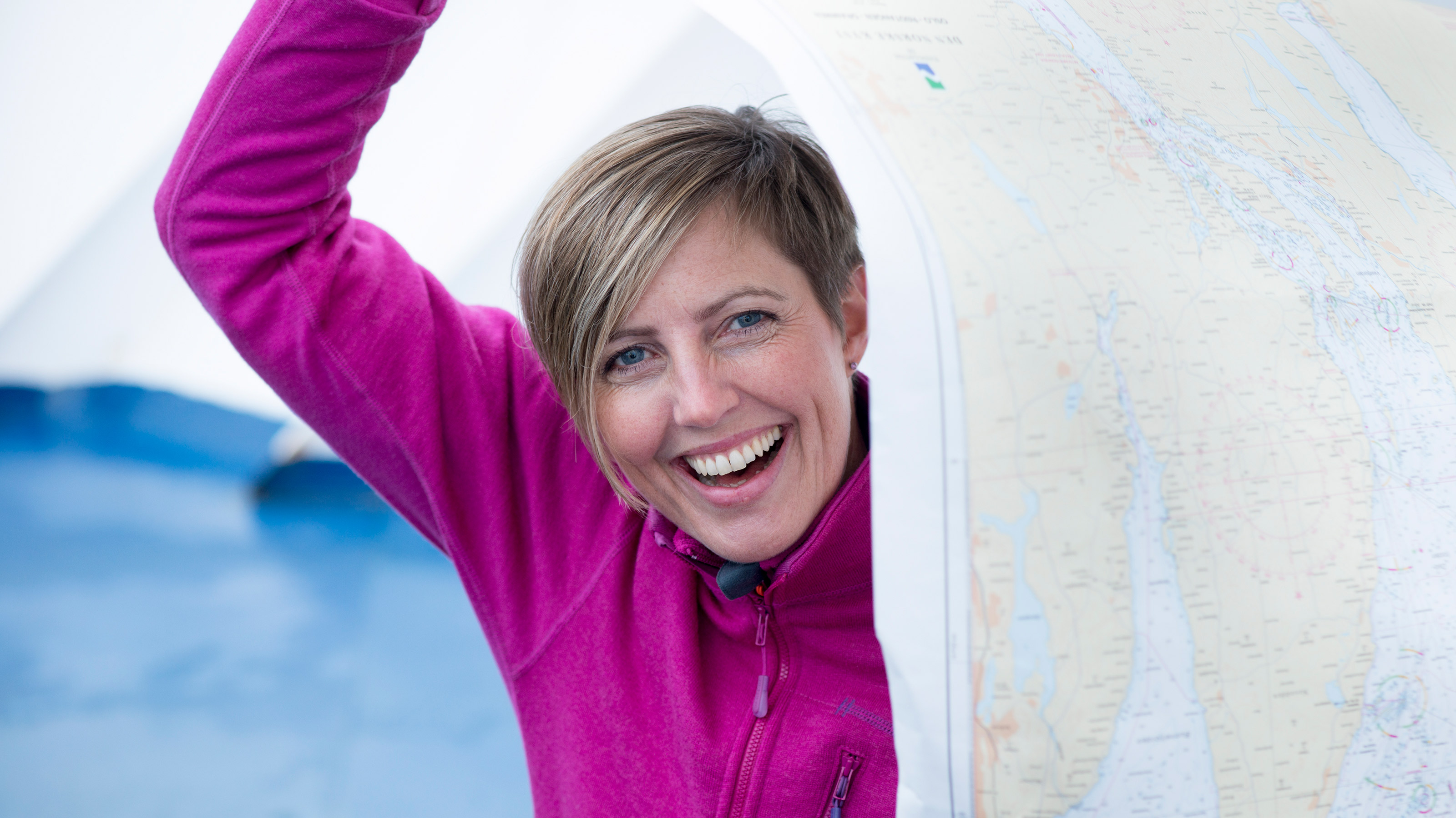 Smilende dame med kort hår og rosa jakke holder et papirsjøkart delvis over hode og kropp. Foto: Morten Brun