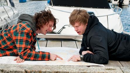 To menn ligger på brygga i ei småbåthavn og peker i et sjøkart. Foto: Morten Brun