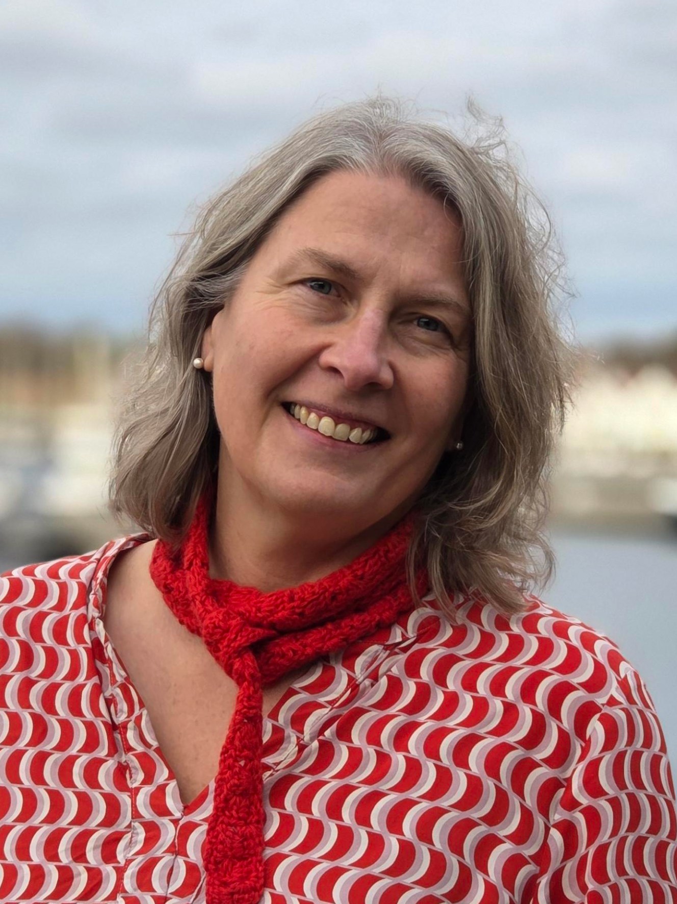 Kvinne i r&oslash;d og hvit bluse smiler.