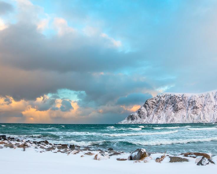 Vintermorgen på en strand i Lofoten. Det er lavvann og bølger slår mot land. Foto: Mostphotos